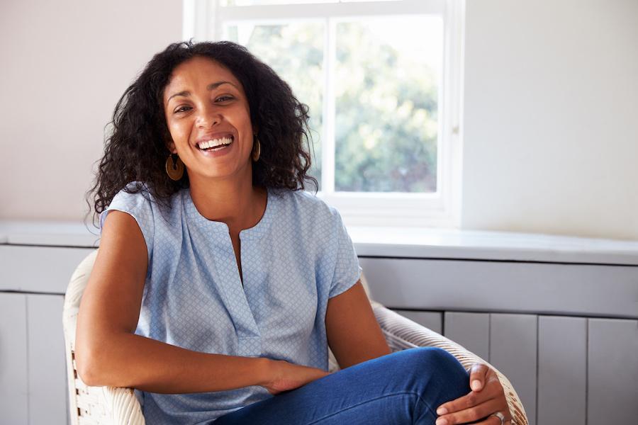 A woman sitting by a bright window, smiling and relaxed
