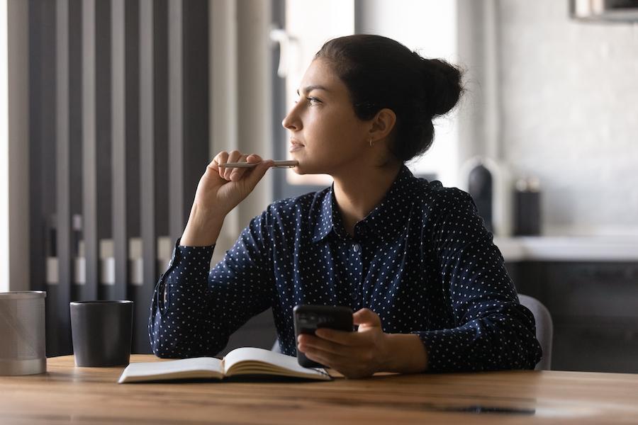 A woman sitting at a desk, pausing to reflect while writing in a notebook